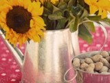 a simple rustic rehearsal dinner centerpiece of a silver teapot, sunflowers and nuts in a bowl is lovely