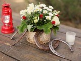a cute bbq rehearsal dinner centerpiece of a simple flower arrangement with berries, horseshoes, a candle lantern and a candle