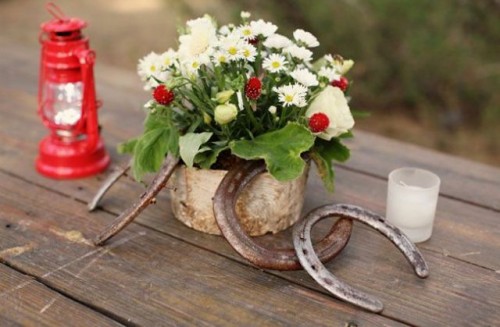 a cute bbq rehearsal dinner centerpiece of a simple flower arrangement with berries, horseshoes, a candle lantern and a candle