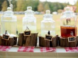 a rehearsal dinner drink station of large tanks placed on tree stumps, with chalkboard signs and plaid napkins is a lovely rustic idea