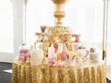 a glam candy bar with a gold sequin tablecloth, a large vase on top and lots of jars and vases