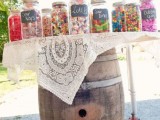 a very simple candy bar made of an old barrel and a tabletop covered with a lace tablecloth plus candies in jars