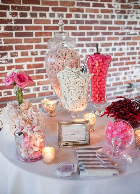 a small candy table with pink blooms, candles and some candies in various jars