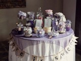a simple and cute candy bar with a table covered with a lavender tablecloth, a banner and lilac jars and bowls with sweets