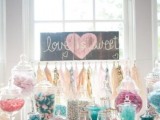 a fun candy table with an inlay dresser, colorful candies in sheer jars, a sign and a bright tassel garland