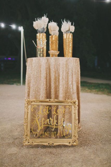 a table with a sequin tablecloth, sparklers and blooms and a lovely sign in a chic gold frame is a lovely idea for a wedding
