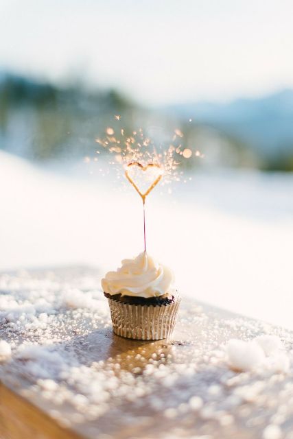 a cupcake with frosting topped with a heart-shaped sparkler is a lovely wedding dessert idea to rock