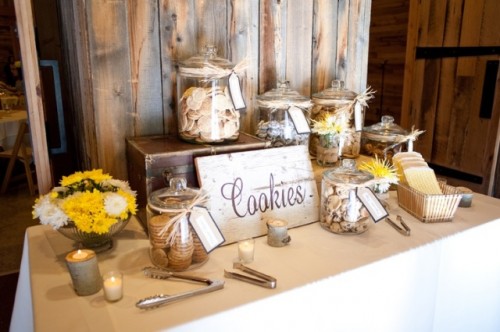 a simple rustic cookie bar with a small chest as a stand, large cookie jars with tags, a basket, candles and blooms