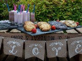 a small cookie bar ona  wooden crate, with a burlap banner, elegant stone trays with cookies and berries and milkshakes