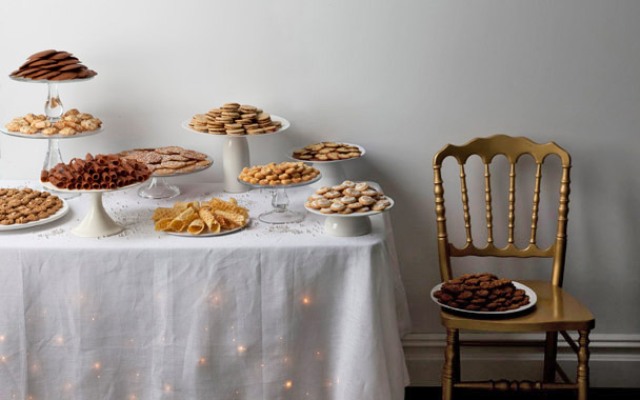 a vintage inspired cookie table with a tablecloth and lights plus simple stands with cookies and sweets