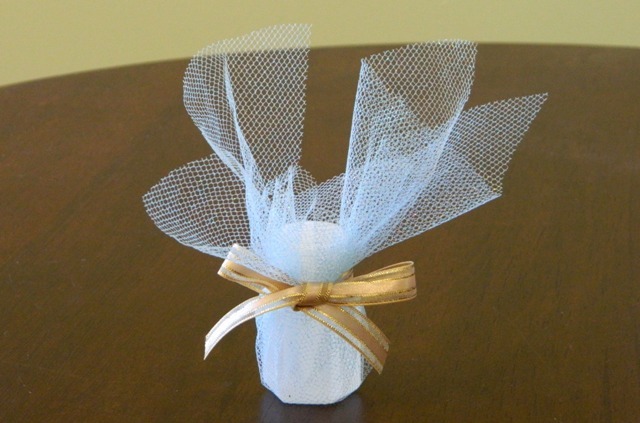A wedding favor   a candle with white tulle plus a mustard ribbon bow for a cozy wedding