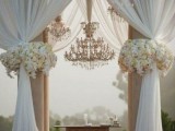 a refined ceremony space with tulle curtains, a large chandelier and lush neutral florals