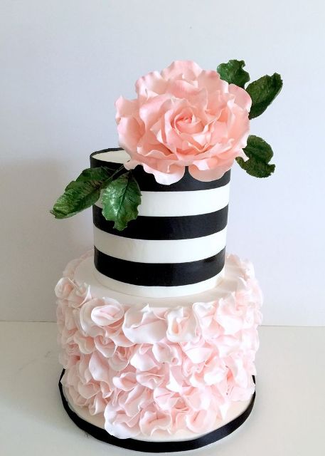 a romantic wedding cake witth a pink floral tier and a black and white one, a pink sugar bloom and leaves on top is a lovely idea for spring or summer