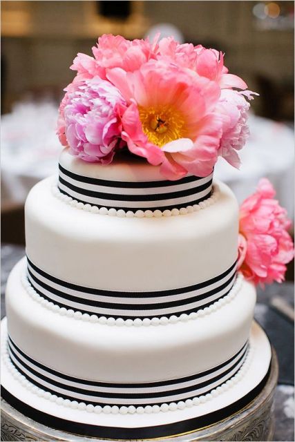 a white wedding cake decorated with black and white ribbons and with pink blooms on top is a lovely idea for a modern wedding with a touch of color