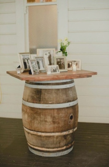 a lovely wedding decoration of a wine barrel and a countertop and lots of family pics and greenery is amazing for a rustic wedding