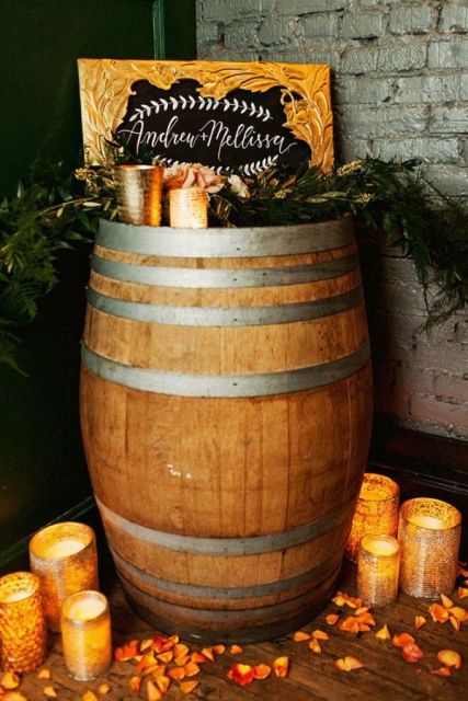 rustic wedding decor of a wine barrel, candles and greenery, with signs and petals on the floor is chic and cool
