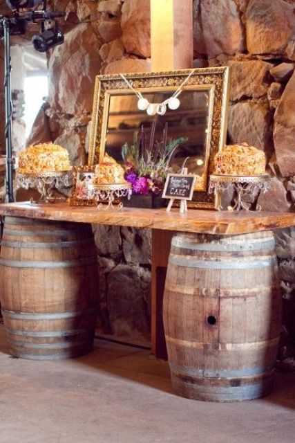 a wedding dessert bar with wine barrels and a countertop, a mirror in a refined frame and lots of various desserts