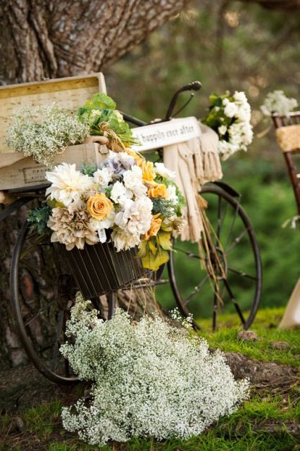 a vintage bike decorated with lush blooms and greenery, with a box filled with greenery and blooms, a blanket and a sign is a simple and lovely decoration