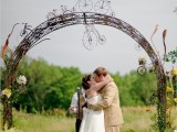 a creative vine wedding arch decorated with white and yellow blooms, greenery and mini bikes to show that the couple loves cycling