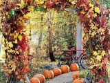 a fantastic lush fall wedding arch covered with bold leaves and a path lined up with pumpkins is a cool idea for a rustic fall wedding