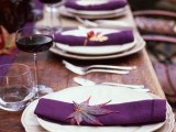 an elegant fall wedding tablescape with an uncovered table, white porcelain, purple napkins and fall leaves accenting them
