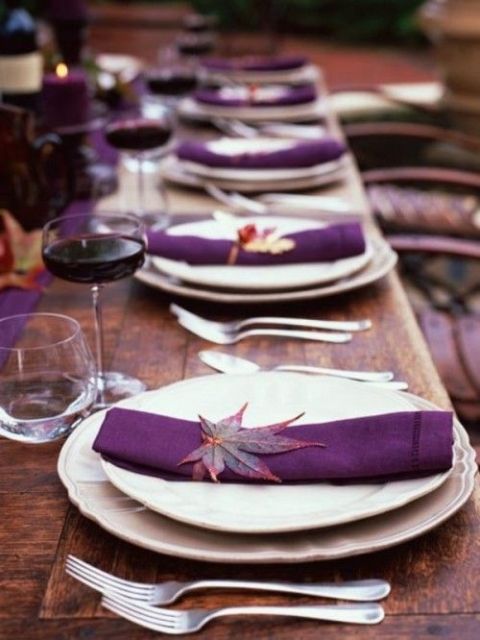 an elegant fall wedding tablescape with an uncovered table, white porcelain, purple napkins and fall leaves accenting them