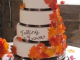 a white wedding cake with ribbon, bold fall leaves and cake toppers is a lovely idea for a modern wedding in the fall