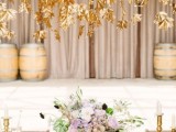 a neutral wedding tablescape with a lilac and white floral centerpiece and gold leaves hanging over the table is a lovely idea for a fall wedding