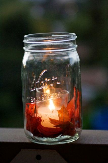 a fall candle lantern of a larger jar with fall leaves and a candle in a smaller glass inside is a very cozy idea for a fall wedding