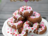 a stack of chocolate donuts with glazing and pink heart sprinkles and a topper is a cool substitute for a usual wedding cake