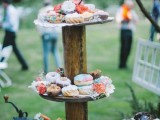 a rustic stand of a tree trunk and wooden tiers with lots of glazed donuts and some frehs blooms for a festival wedding