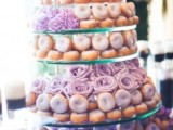 a multi-tier glass donut stand with various types of glazed donuts and blooms are a cute way to serve them