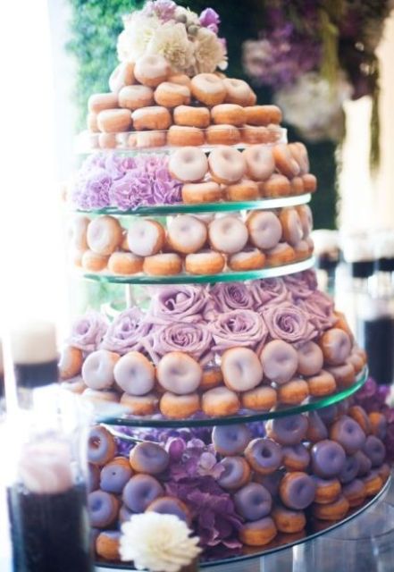 a multi-tier glass donut stand with various types of glazed donuts and blooms are a cute way to serve them