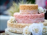 a round krispie rice wedding cake with a pink tier, lace ribbon and white blooms