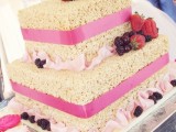 a square krispie rice wedding cake with pink ribbons, pink silk and lots of fresh berries on top