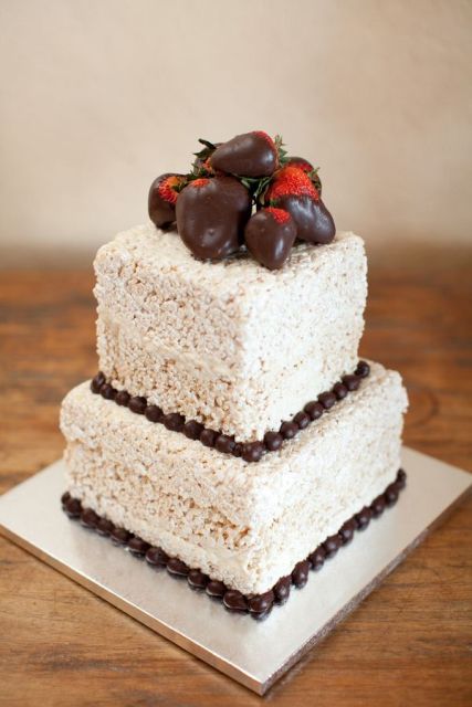 a square krispie rice wedding cake with chocolate decor and some strawberries in chocolate on top