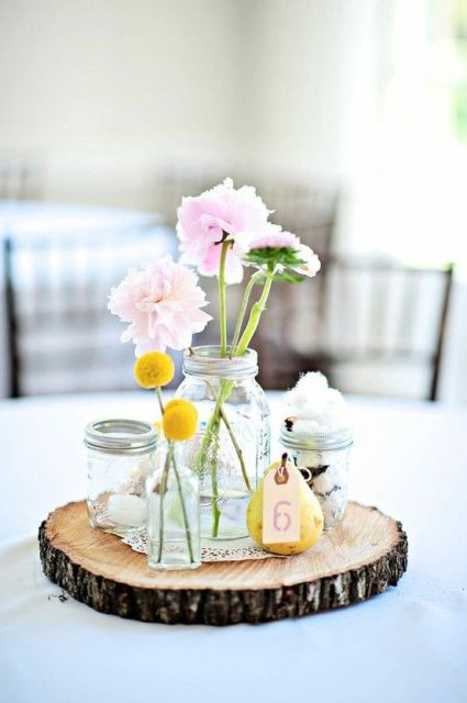 a cluster wedding centerpiece of a wood slice, jars with pink blooms and billy balls, a pear with a table number is a lovely idea