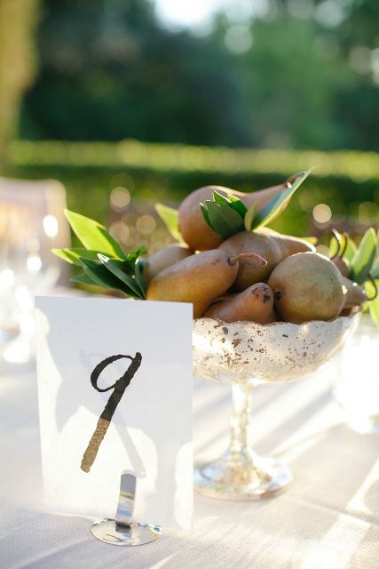 an edible wedding centerpiece of a metallic bowl with pears and foliage plus a table number is a stylish and easy idea for a fall wedding