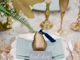 a chic wedding tablescape with a grey and gold printed tablecloth, gold goblets, candleholders and a gilded pear as a wedding favor that adds more chic to the table
