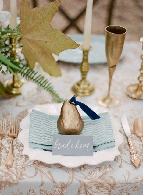 a chic wedding tablescape with a grey and gold printed tablecloth, gold goblets, candleholders and a gilded pear as a wedding favor that adds more chic to the table