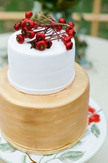 an elegant white and gold wedding cake topped with berries is a stylish winter wedding dessert