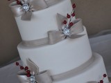 a white wedding cake decorated with ribbon bows, brooches and red berries for a formal winter wedding