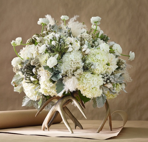 A unique winter wedding centerpiece of white blooms, pale greenery placed on gilded antlers is a very stylish and chic idea