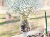 a pretty winter wedding centerpiece of a black table runner, a wood slice, a vase with pinecones and baby’s breath is very chic