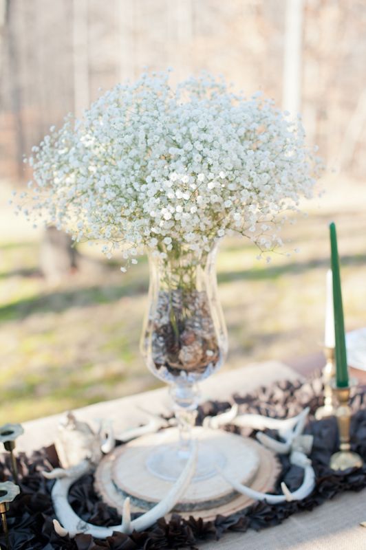 A pretty winter wedding centerpiece of a black table runner, a wood slice, a vase with pinecones and baby's breath is very chic