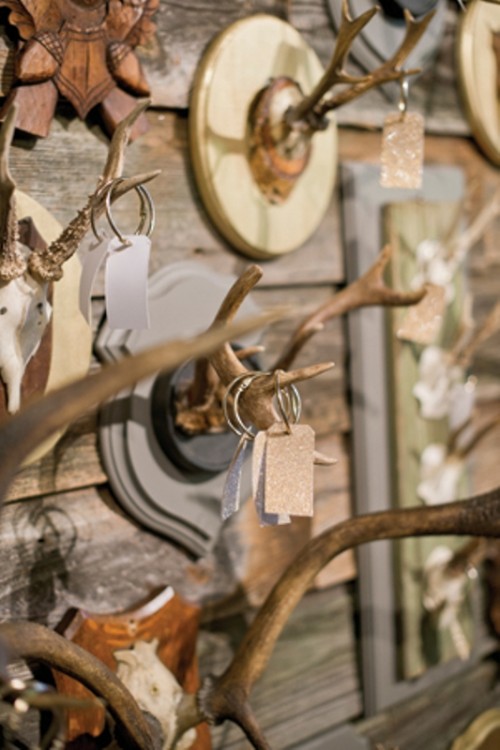 a wall with antlers used as holders for seating cards is a creative idea for a woodland wedding