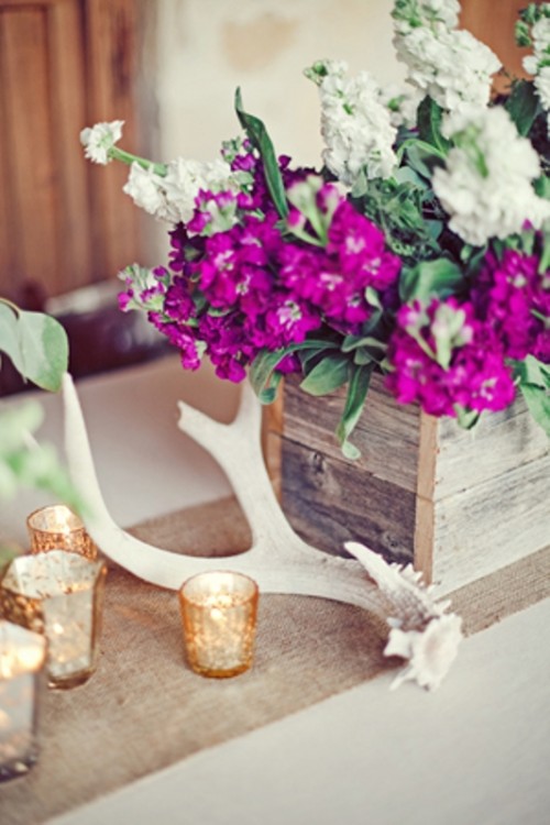 a rustic centerpiece of a burlap runner, antlers, candles and a reclaimed wood box with super bright flowers is very cool and bold
