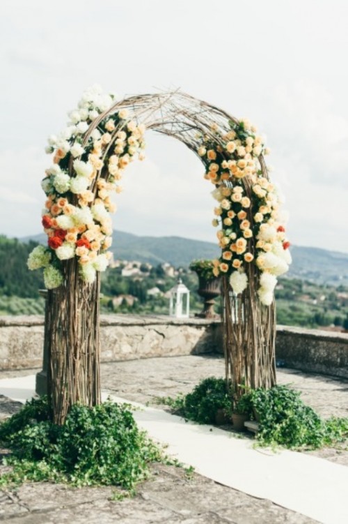 a stylish wedding arch made of branches, white, peachy and coral blooms and greenery at the base
