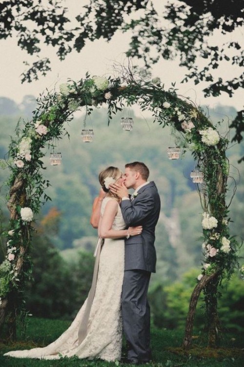a beautiful wedding arch covered with greenery and white blooms and hanging candleholders is amazing