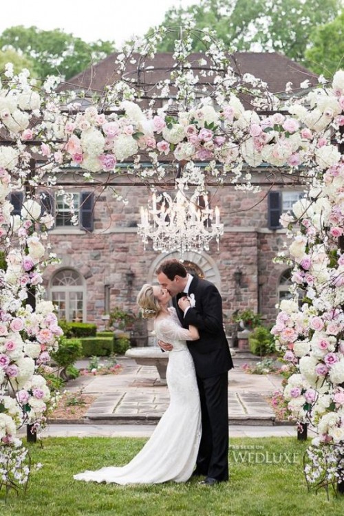 a lush and beautiful wedding arch covered with light pink and white blooms and a crystal chandelier is a stylish and chic idea